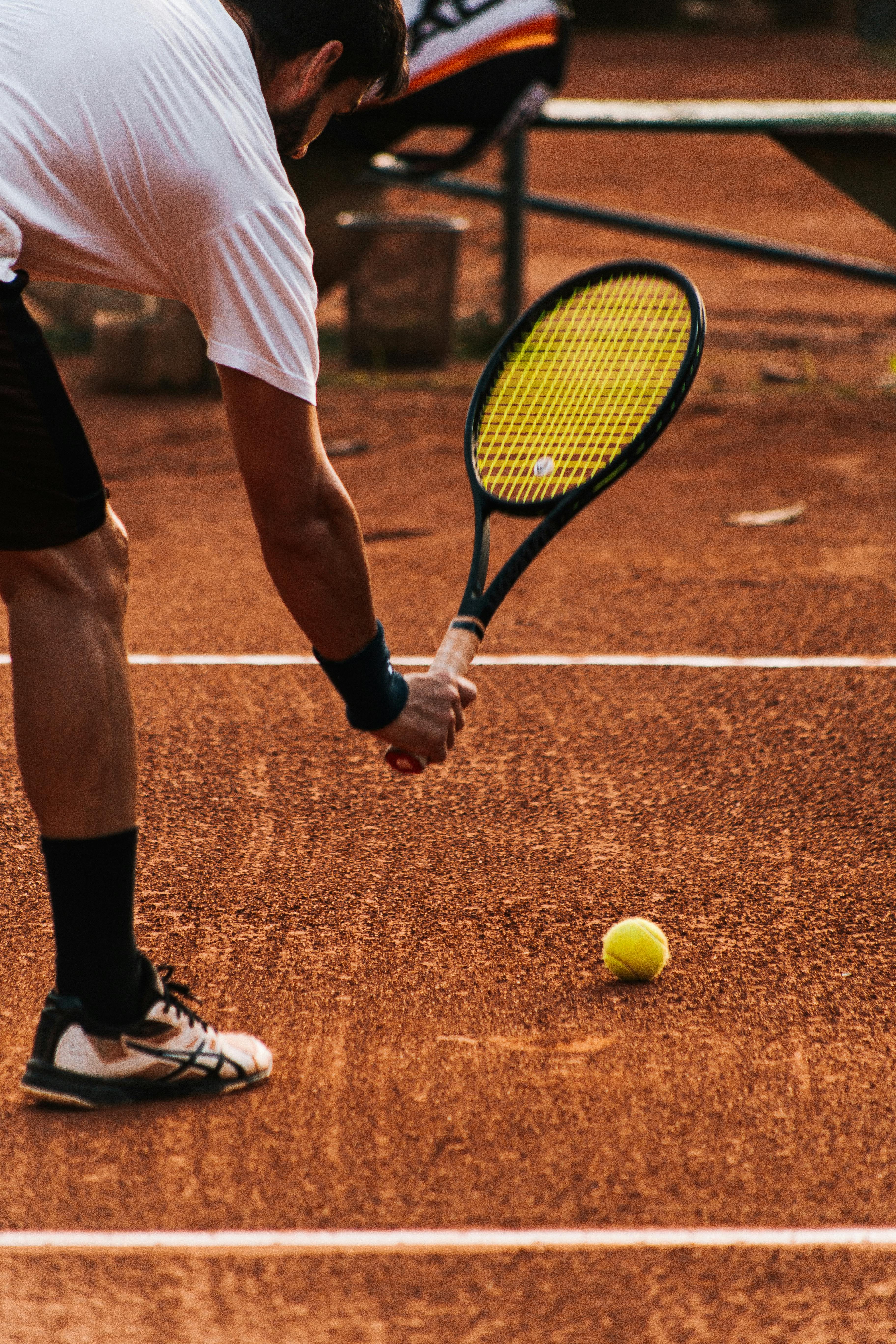 Adult tennis player on clay court getting ready to serve during a sunny day match.